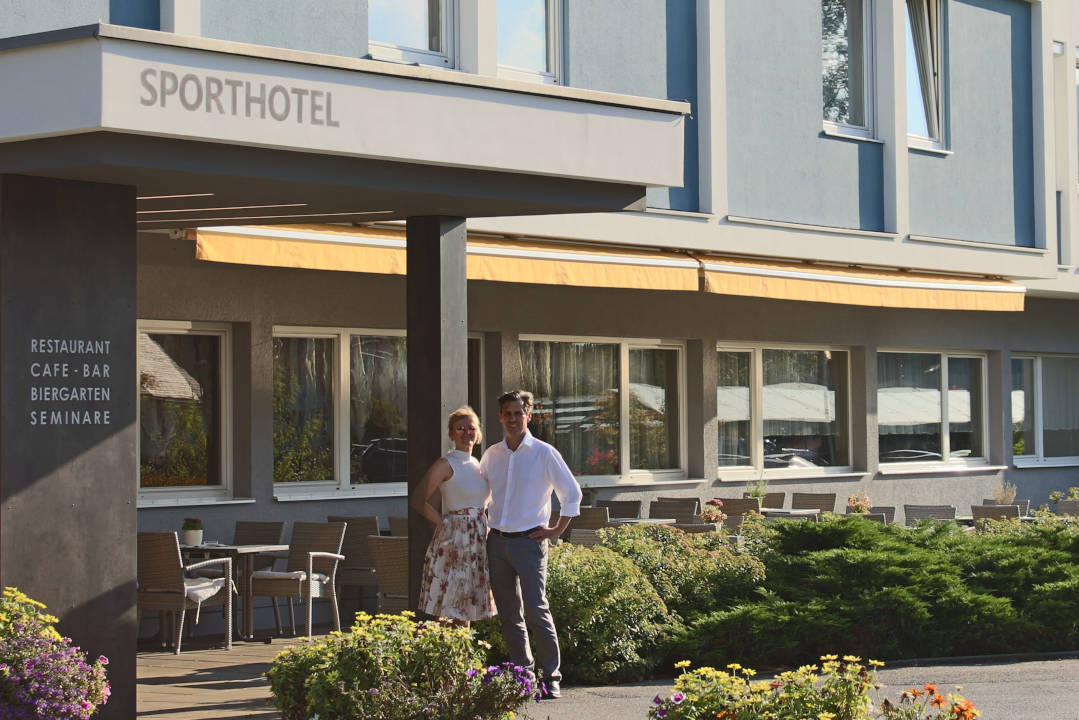 Vorderansicht vom Sporthotel Kapfenberg. Ein Mann und eine Frau stehen vor dem Hotel.